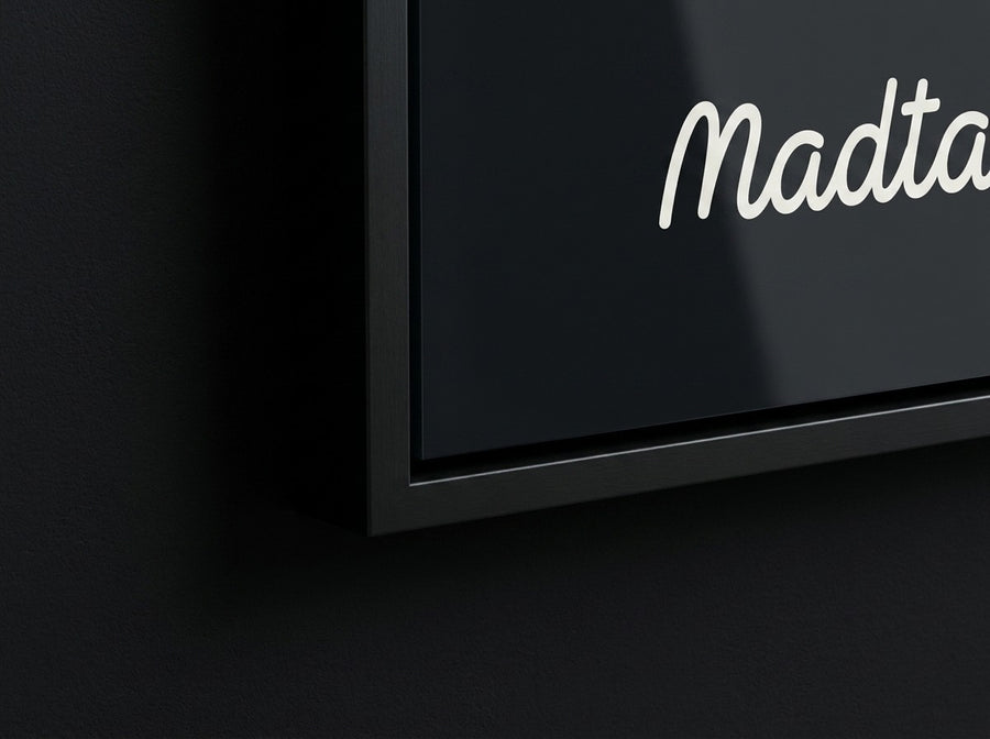 The corner of a Madtag print in a black wood frame, the sheet flush against the moulding behind acrylic, no mount board.